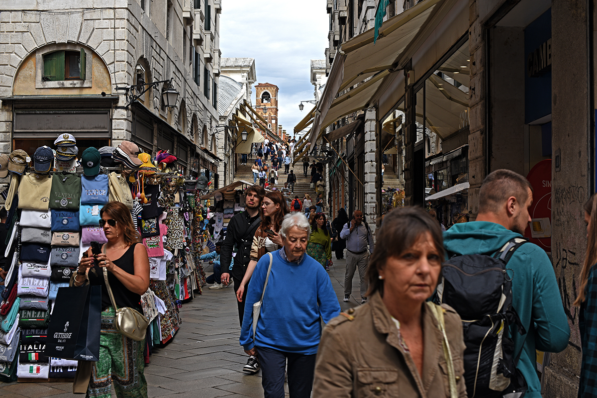 Touristes marchant dans une rue animée près du pont du Rialto à Venise, avec des étals de souvenirs.