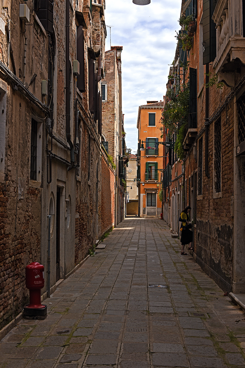 Ruelle étroite et pavée de Venise, bordée de bâtiments anciens et d'une bouche d'incendie rouge.