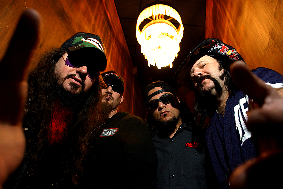 Les membres de Damageplan posent en contre-plongée dans un couloir sombre, éclairés par un lustre, look metal affirmé.