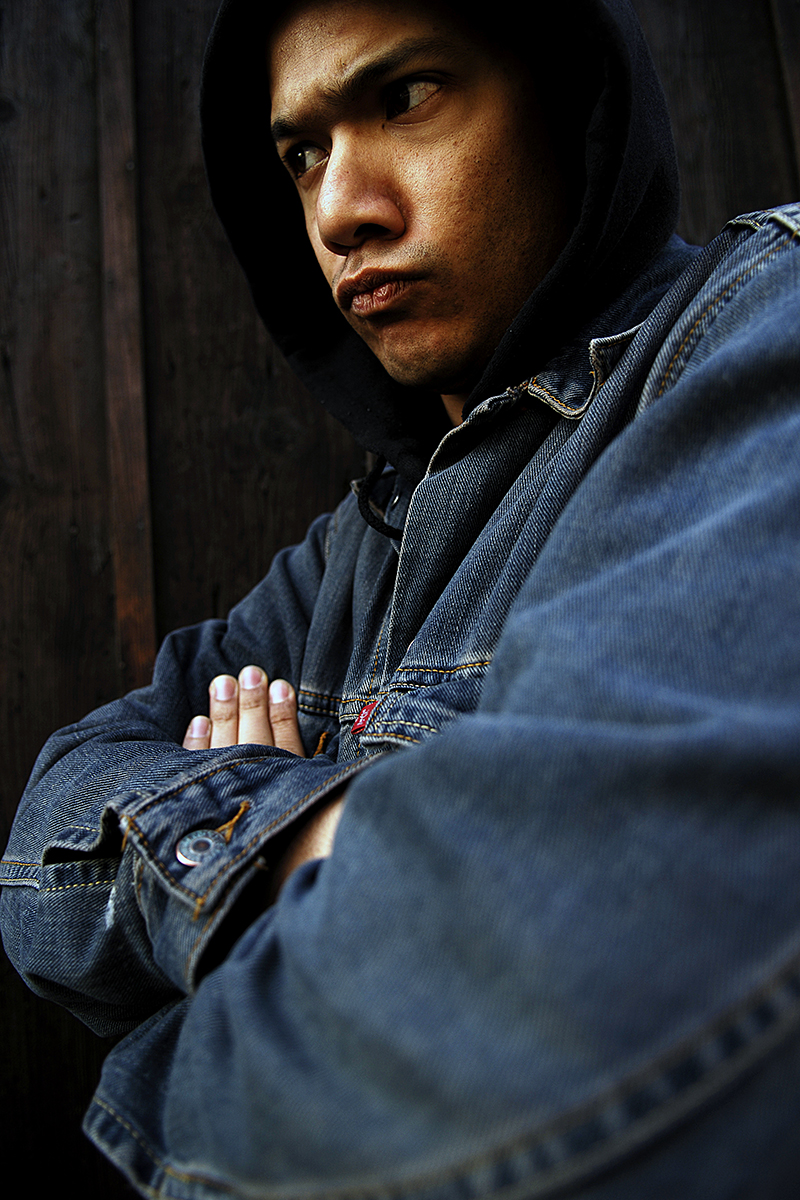 Portrait en contre-plongée de Danko Jones en jean et capuche, bras croisés et regard déterminé