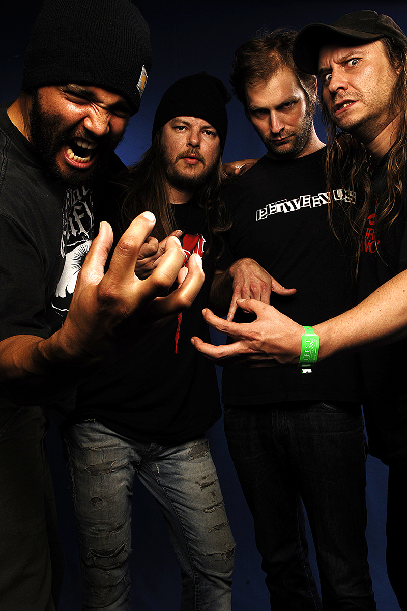 Les membres d’Entombed posent de manière agressive et expressive, vêtus de noir, avec gestes tendus et regards intenses.