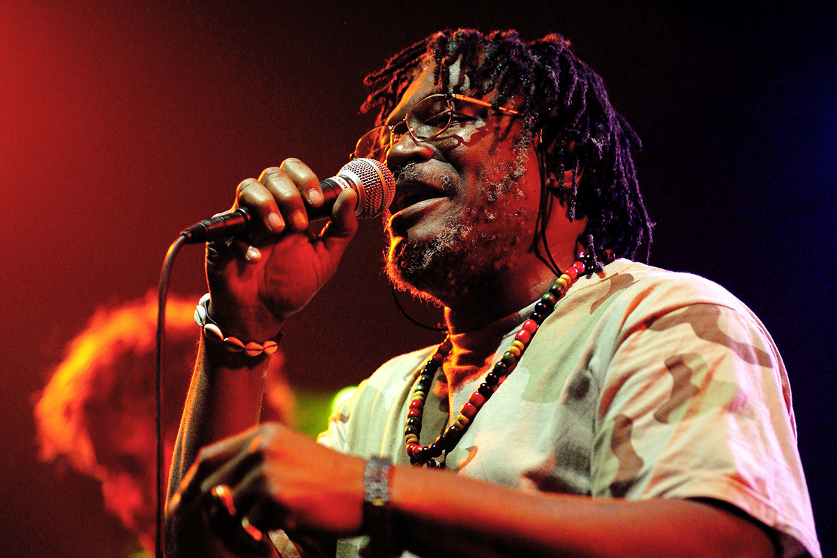Horace Andy chantant sur scène, tenant un micro, éclairé par une lumière chaude et colorée.
