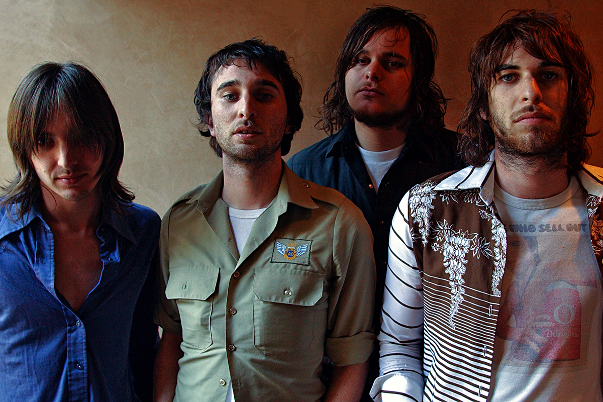 Les quatre membres du groupe Jet posent dans une lumière douce, tenues rétro et ambiance rock années 2000.