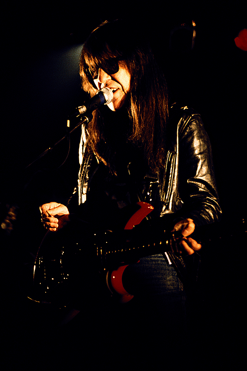 Link Wray sur scène, chantant et jouant de la guitare, en blouson de cuir