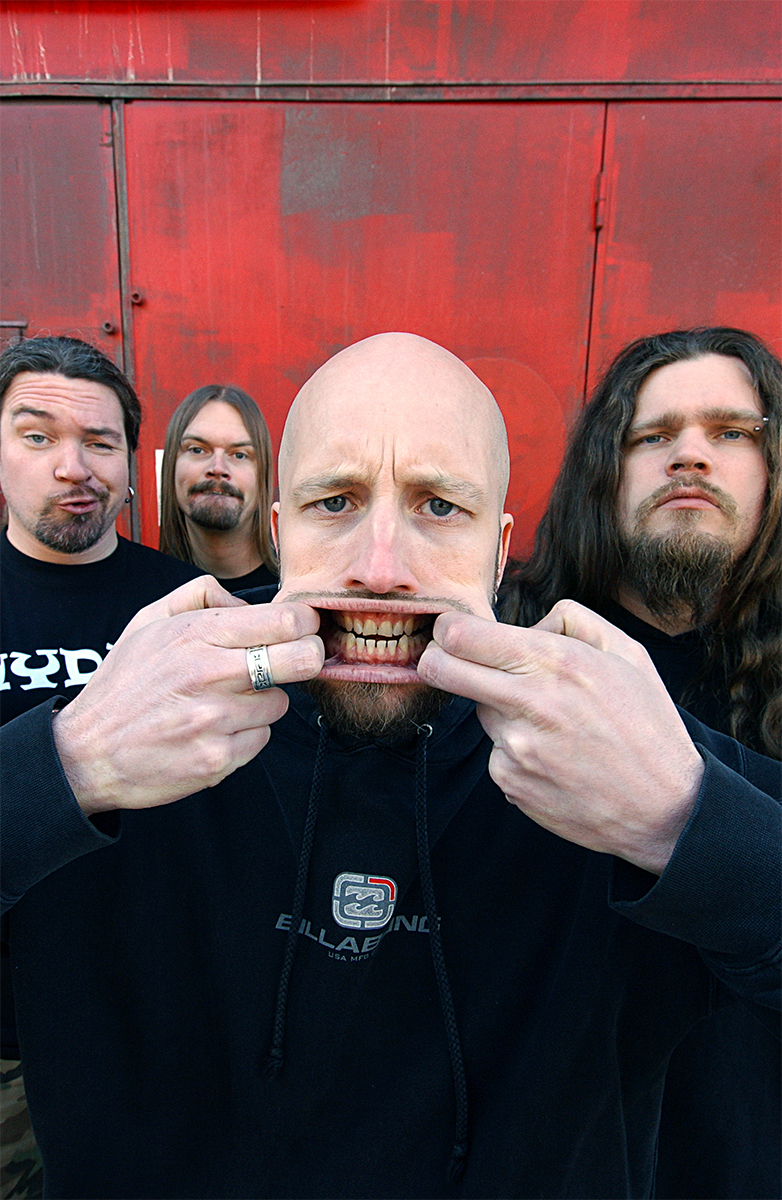 Portrait décalé du groupe Meshuggah devant un mur rouge, le chanteur grimace au premier plan