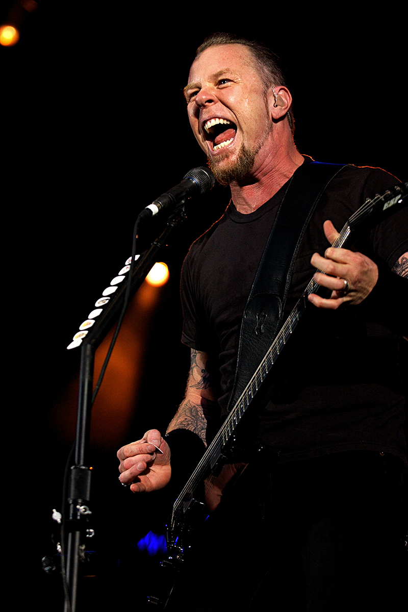 James Hetfield de Metallica en plein chant au Parc des Princes, guitare à la main et lumière de scène en fond.