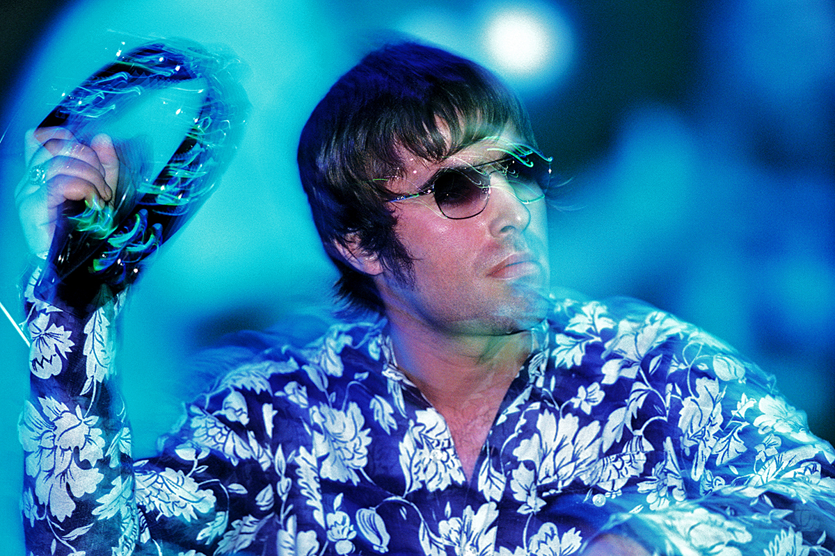 Liam Gallagher, chanteur d’Oasis, portant une chemise à fleurs et des lunettes de soleil, joue du tambourin sur scène au festival Rock in Rio