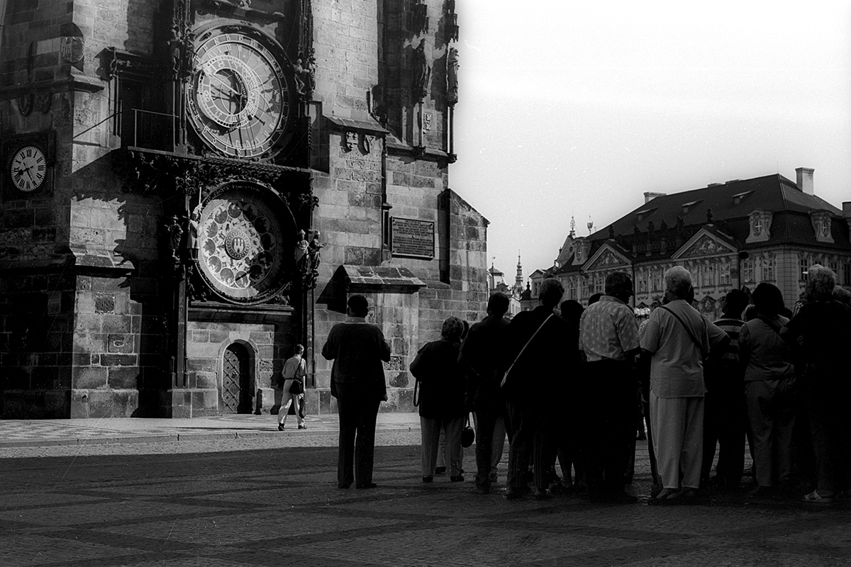 Groupe de personnes observant l'horloge astronomique de Prague à la fin des années 90, avec des bâtiments historiques en arrière-plan.