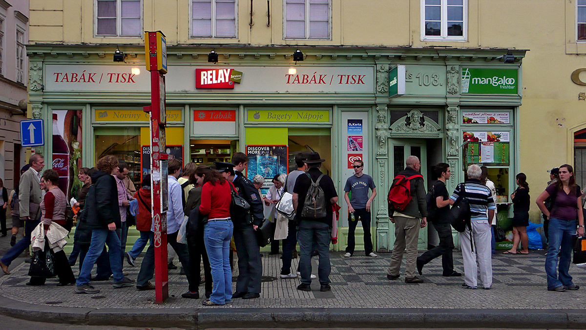 Groupe de touristes devant des boutiques à Prague, montrant l'uniformisation des enseignes commerciales.