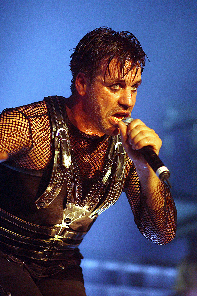 Till Lindemann, chanteur de Rammstein, en pleine performance live avec micro et tenue noire, sueur au front et regard intense