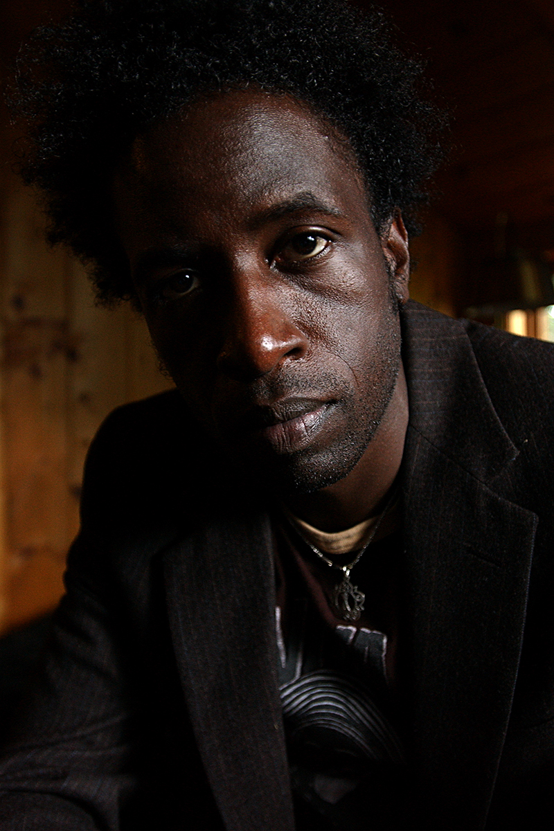 Portrait rapproché de Saul Williams, regard intense vers l’objectif, lumière tamisée