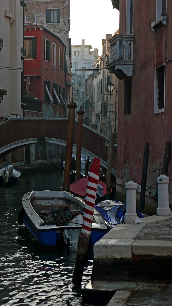 Canal de Venise avec des bateaux amarrés et des bâtiments colorés, sous un pont en pierre.