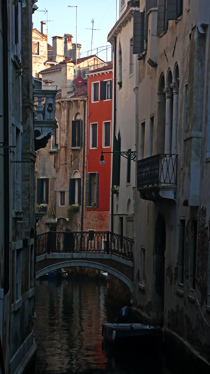Canal étroit à Venise avec un petit pont en pierre et des bâtiments colorés bordant l'eau.