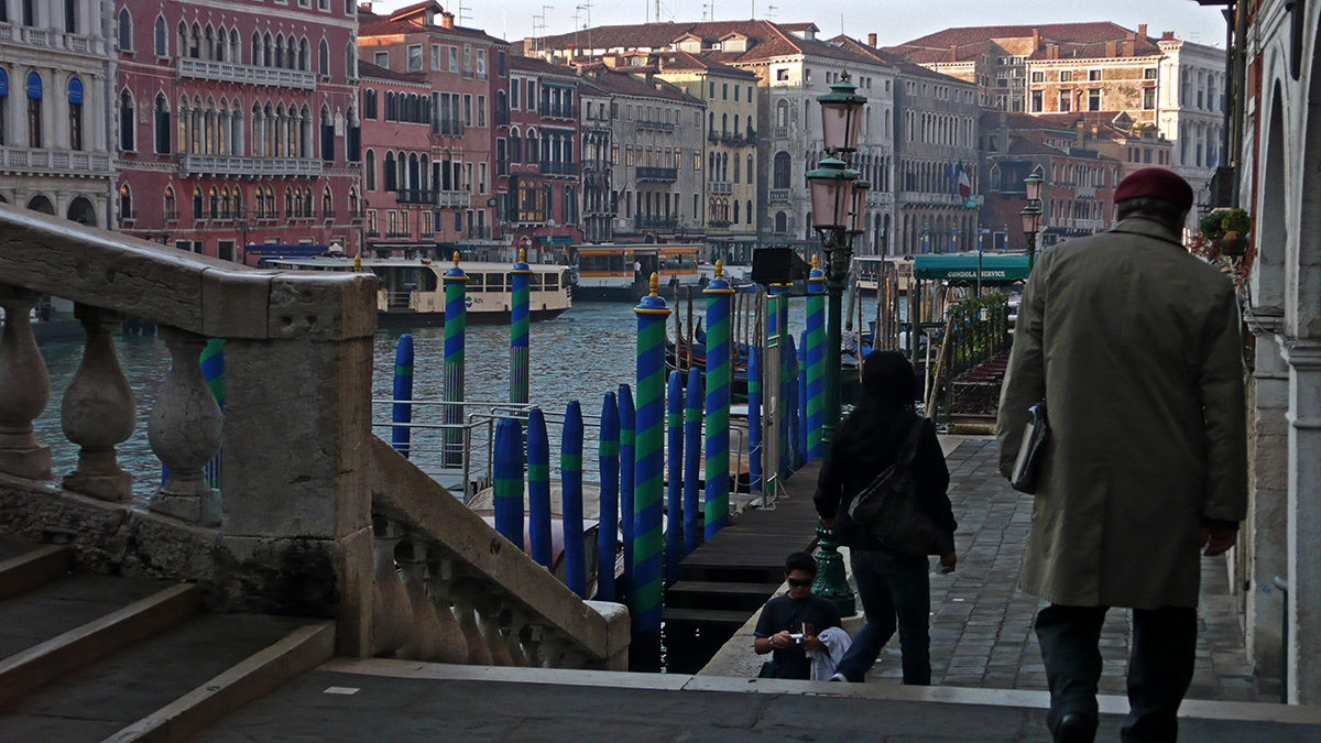 Matin calme sur le Grand Canal de Venise, avec des passants et des bâtiments colorés en arrière-plan.