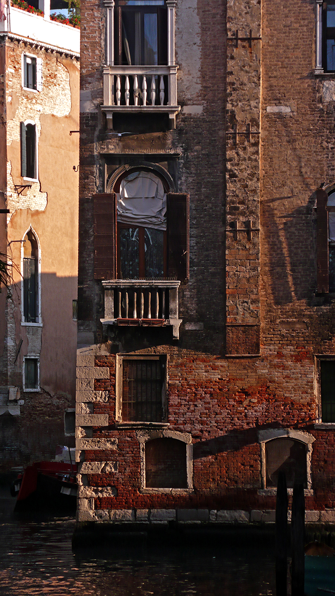 Façades de bâtiments anciens à Venise, avec des balcons en pierre et des volets en bois, bordant un canal.