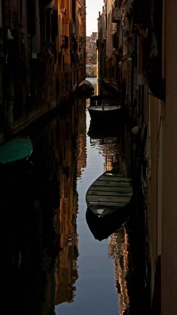 Canal de Venise avec des reflets de bâtiments et des bateaux amarrés, capturant la sérénité de la ville.