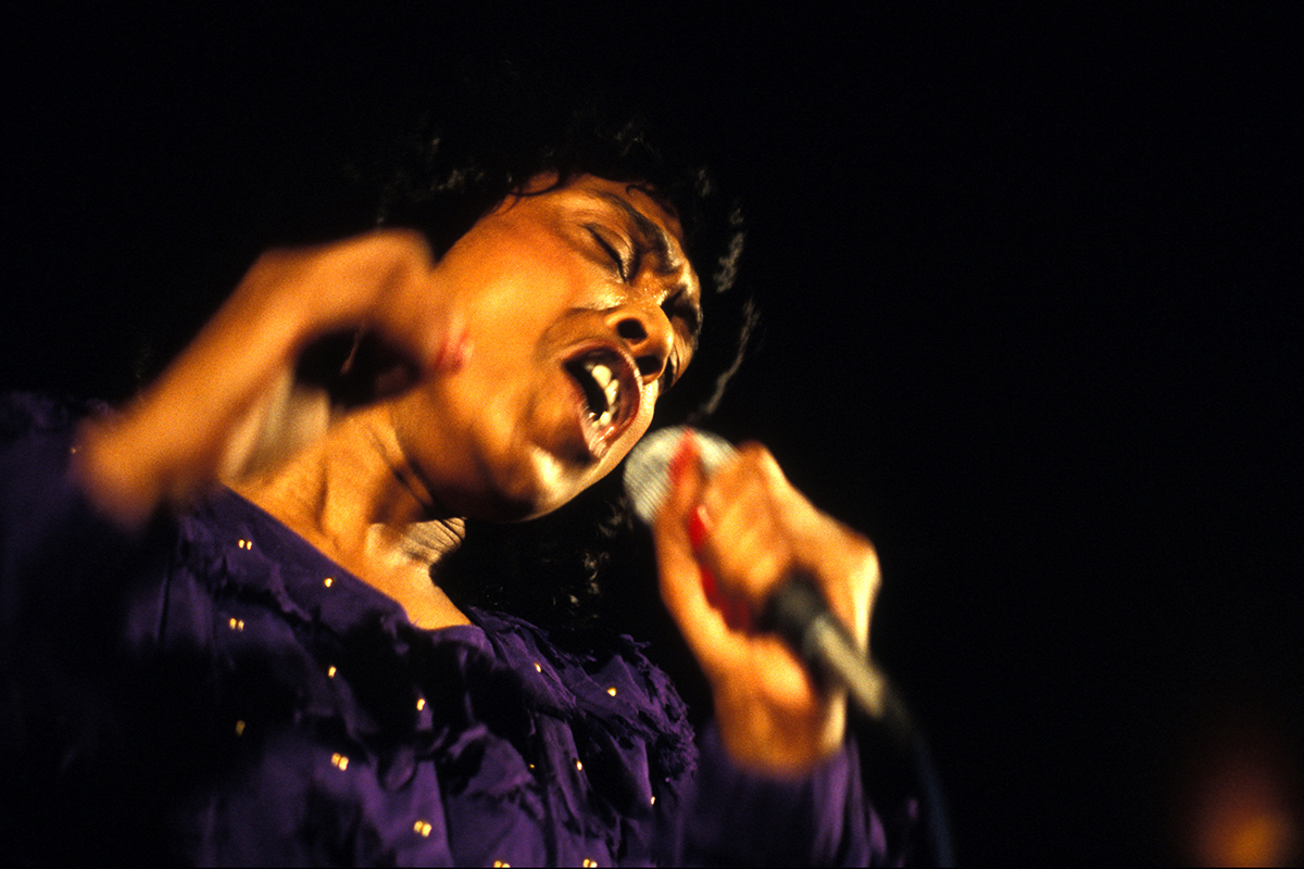 Ann Peebles chantant sur scène avec intensité, micro à la main, dans une lumière tamisée.