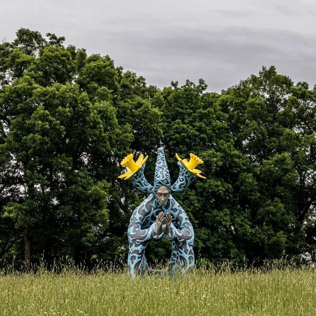 Blue figure with cupped hands and yellow daffodils extending from its ears in Ephemera by Daniel Popper at The Morton Arboretum in Lisle, Illinois