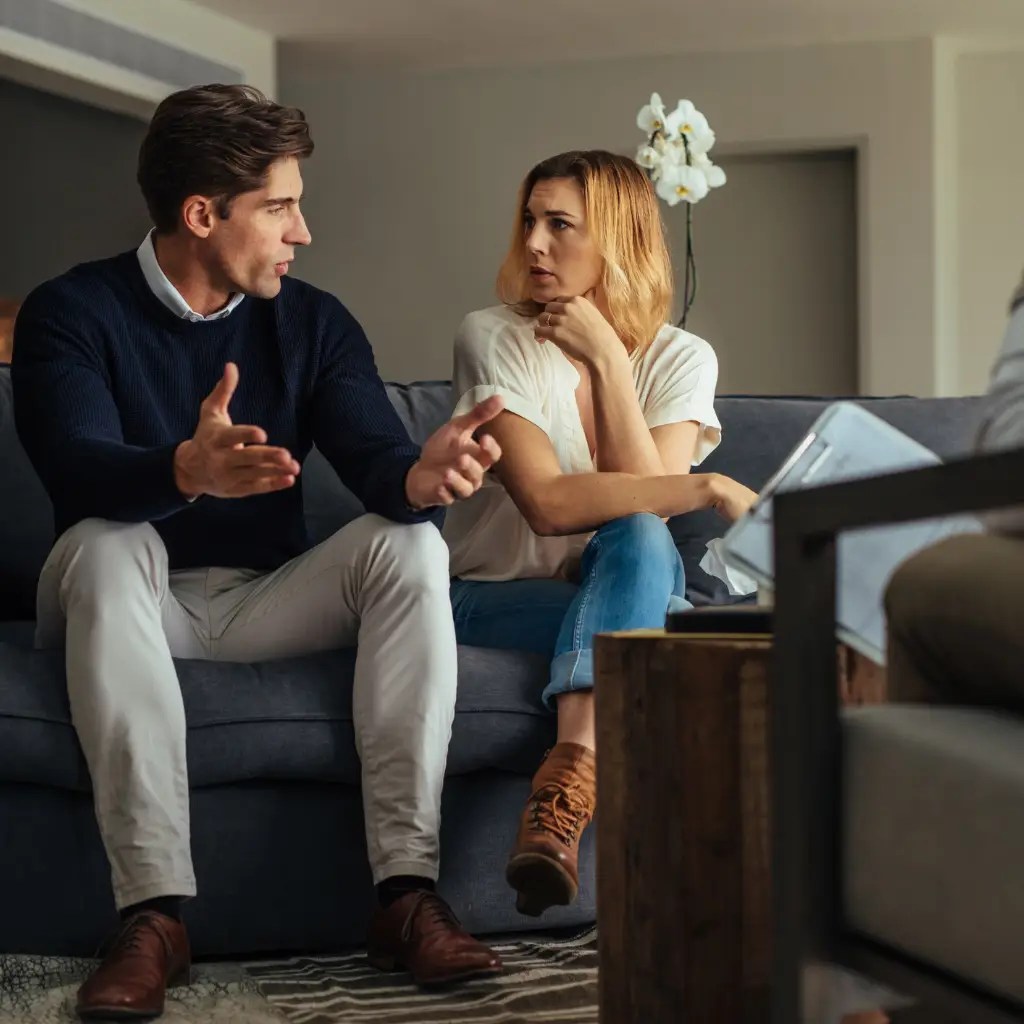 Couple sitting on a couch during a couple counseling session, expressing concerns and working through conflict with a therapist. Marriage counseling Enid OK. Couples counseling Enid OK.