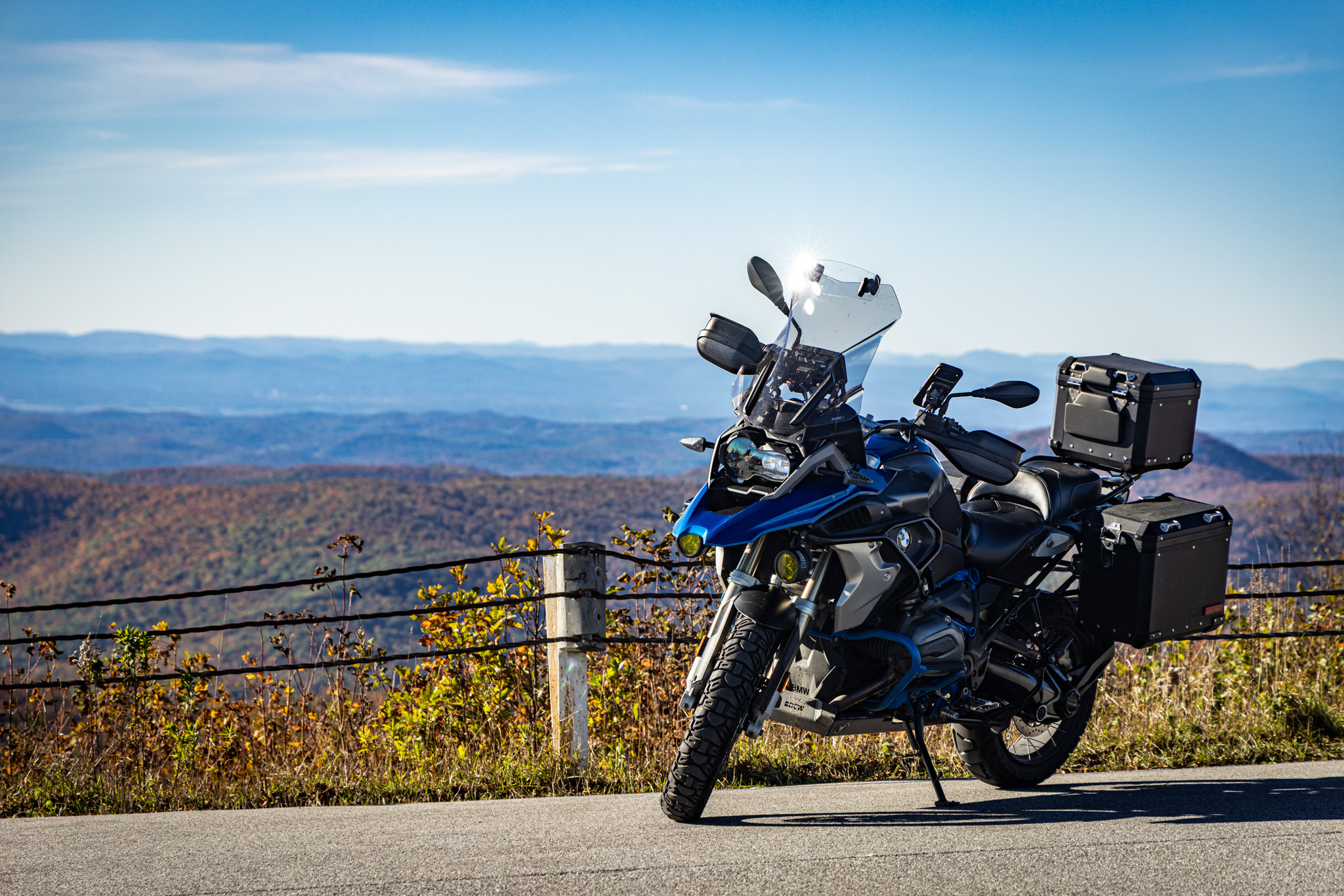 BMW GS parked at the summit fence with distant ridgelines behind it