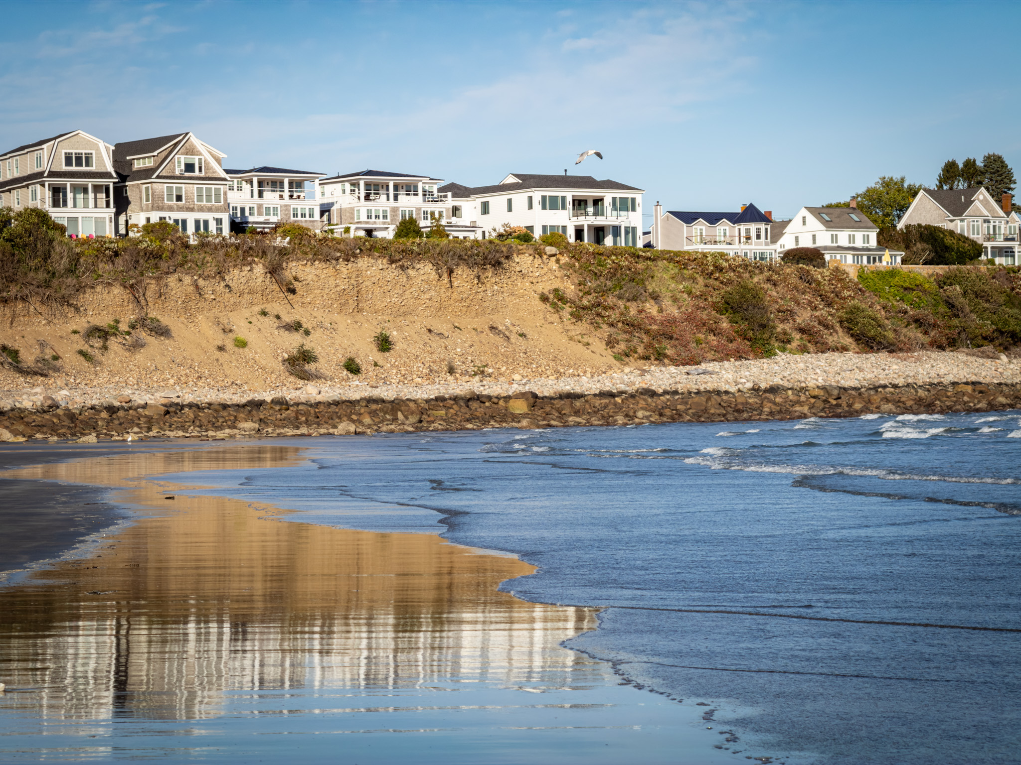 Houses on a bluff reflected in the wet sand at Long Sands Beach