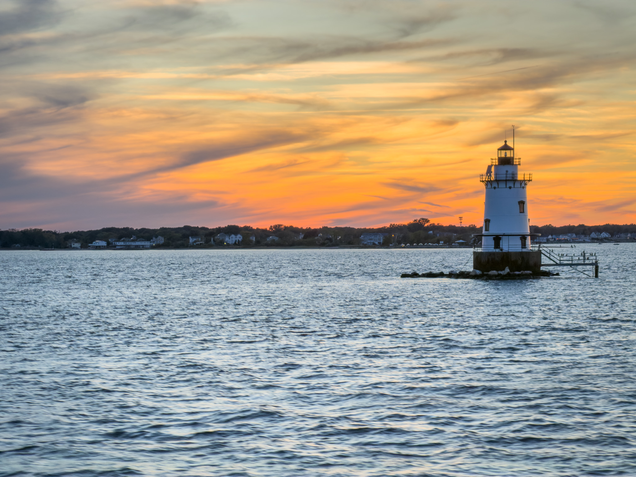 Lighthouse silhouetted against an orange sunset sky
