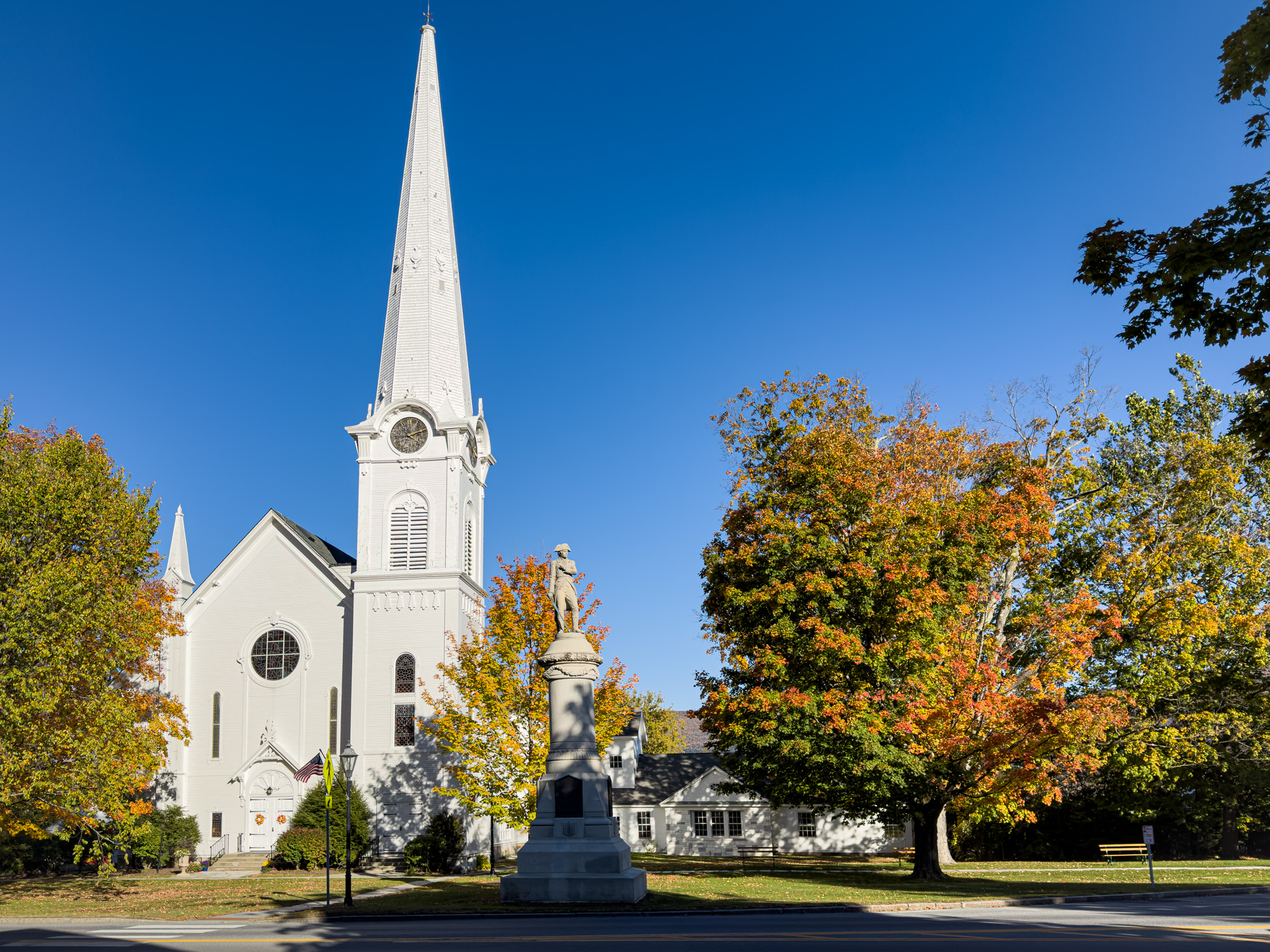 White church steeple behind orange maples near a stone monument