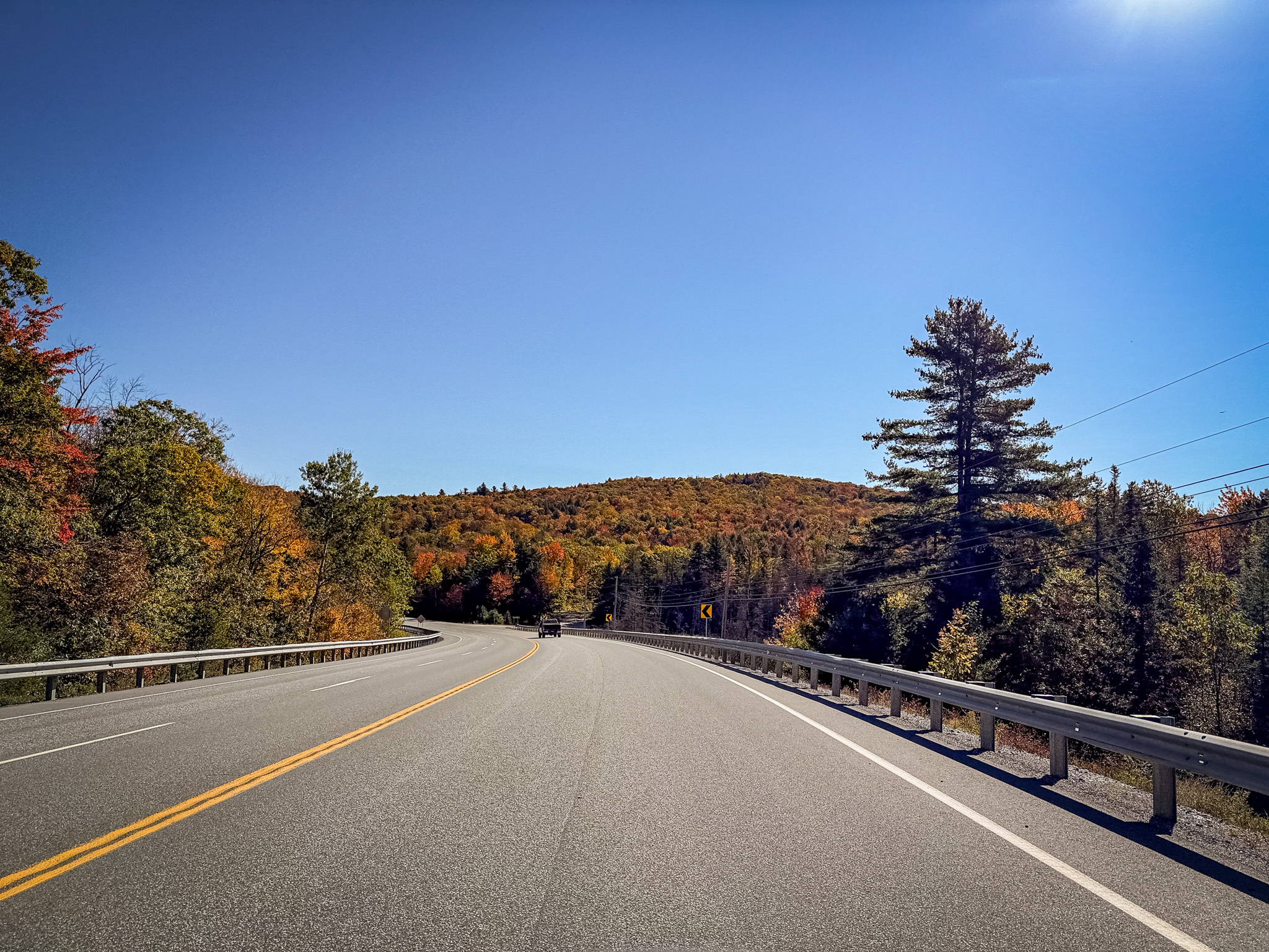 Two-lane highway curving through fall color under a clear blue sky