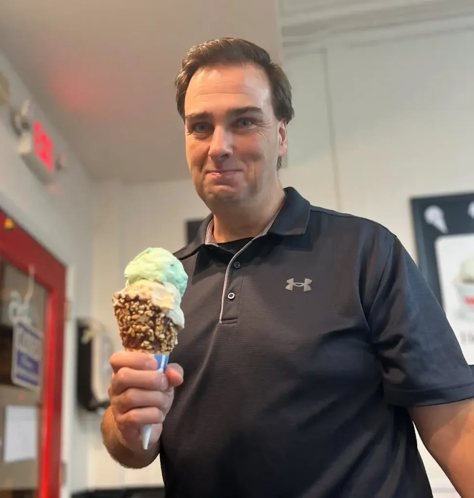 Jason Romans wearing Under Armour polo smiling holding a two-scoop ice cream cone