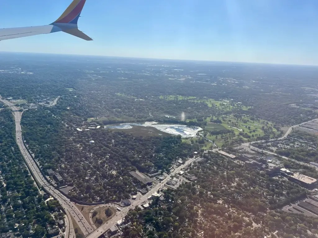 Aerial view including a piece of a Southwest plane wing with urban landscape with roads, trees, and open spaces seen from above
