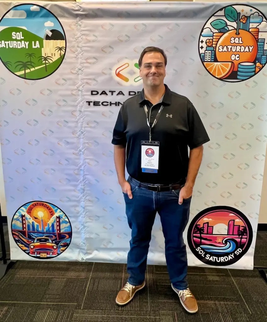 Jason Romans standing in front of a step and repeat banner with logos from the local SQL Saturday