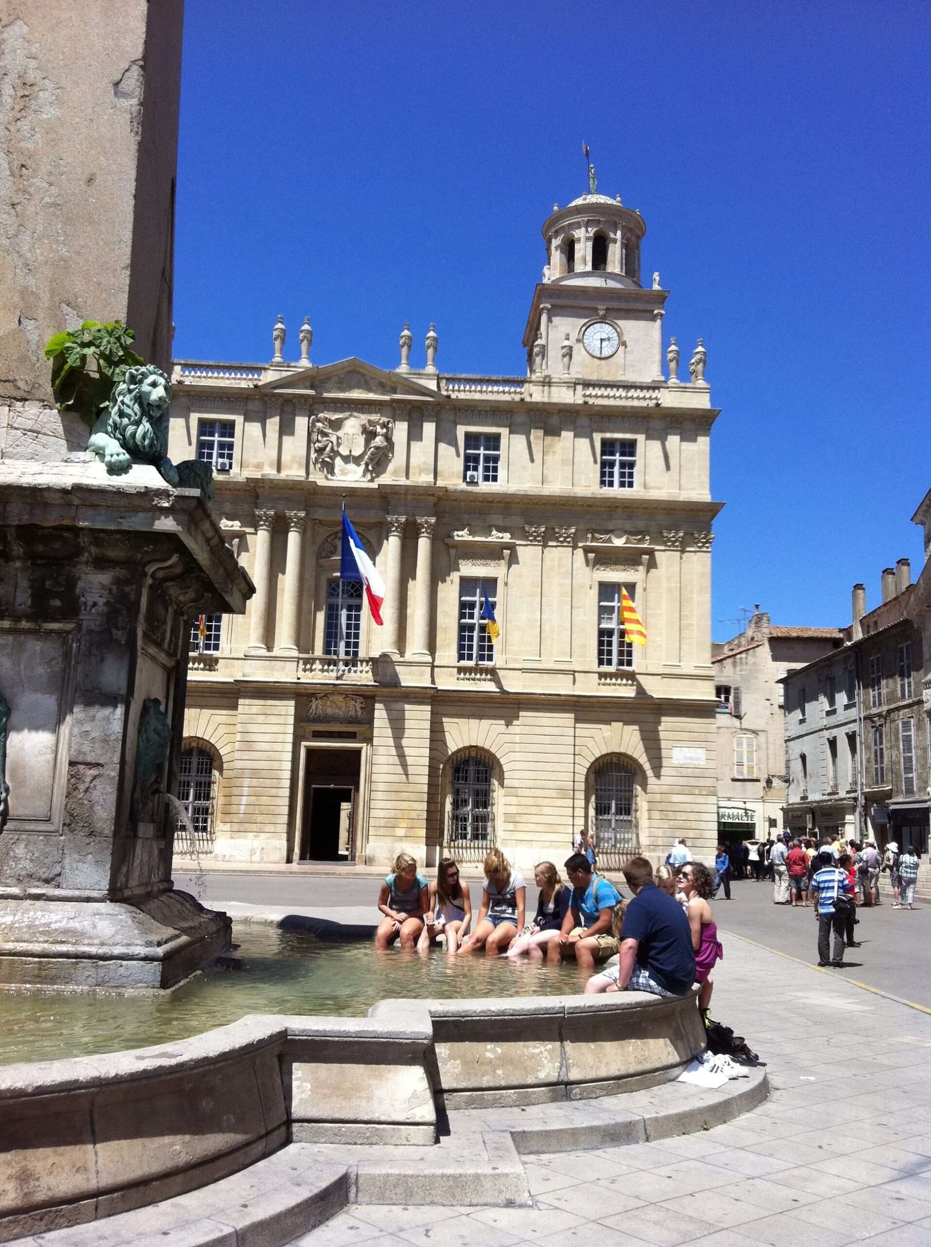 Historic building with clock tower and fountain under clear blue sky.