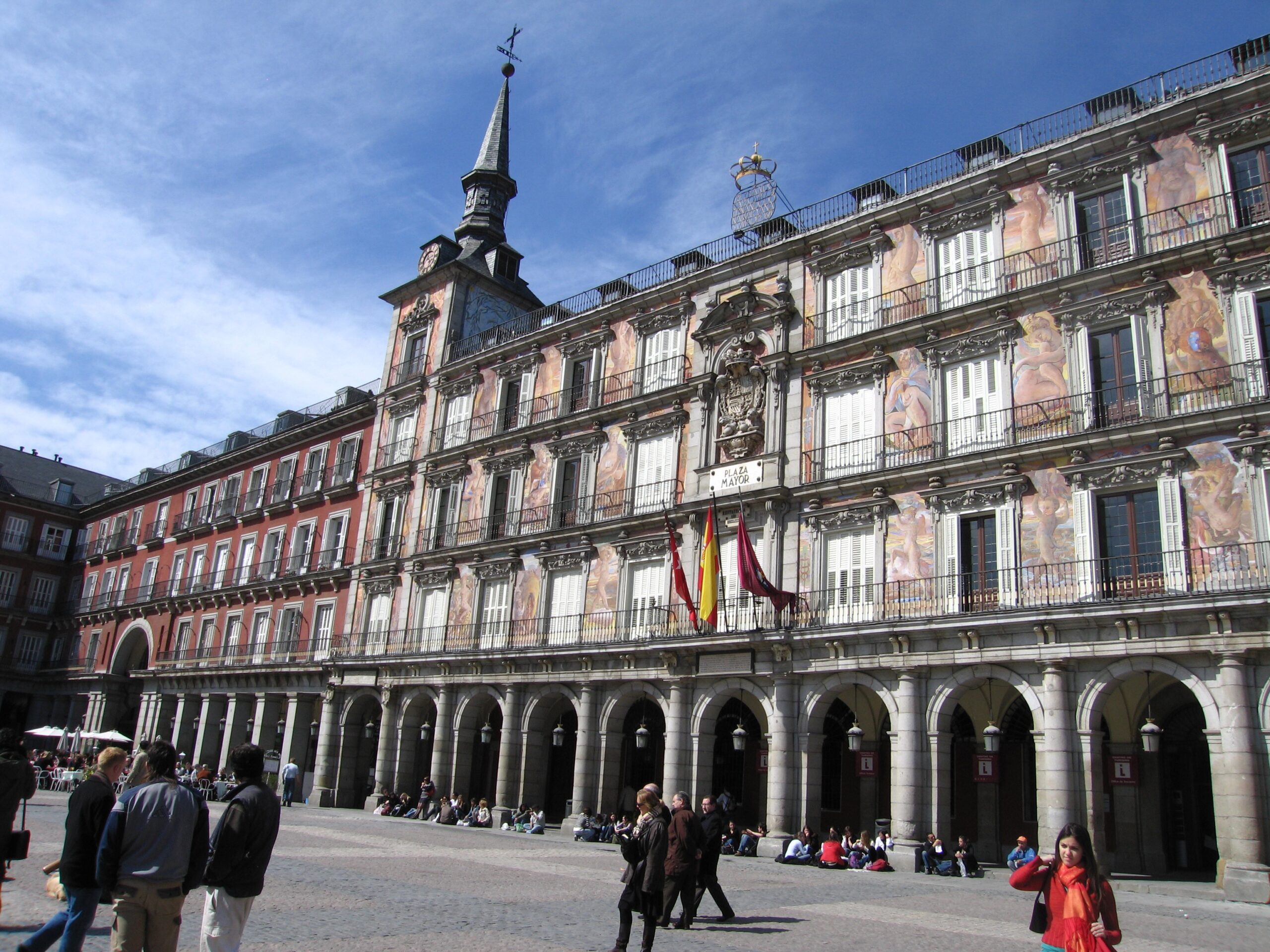 Historic Plaza Mayor in Madrid with people walking and Spanish flags.