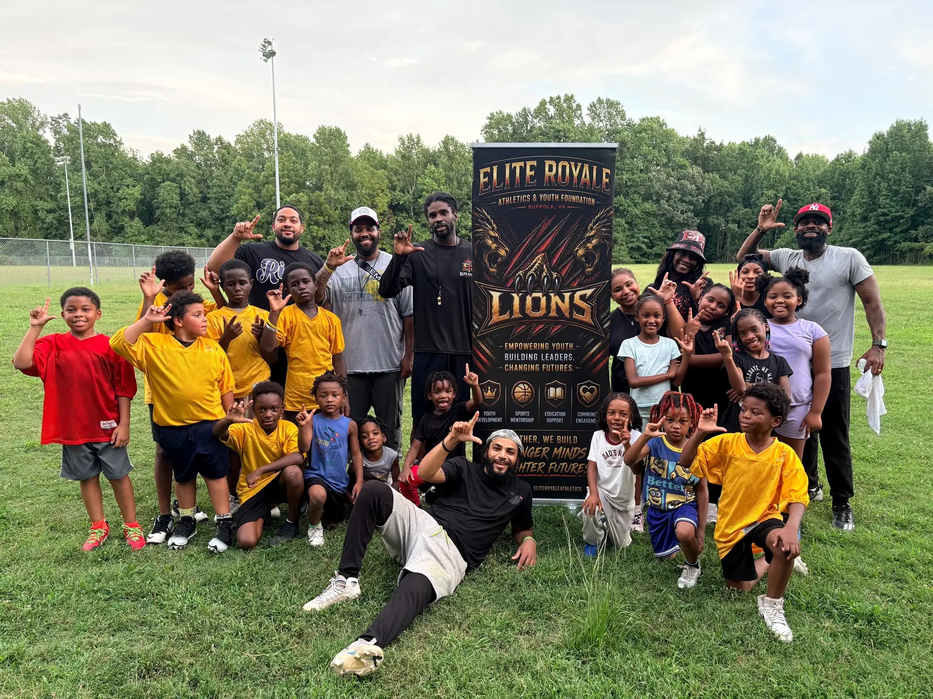 Elite Royale Athletics youth football and cheer team with coaches beside the Elite Royale Lions banner in Suffolk, Virginia