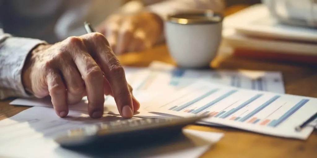 Person reviewing financial documents with a calculator and coffee.