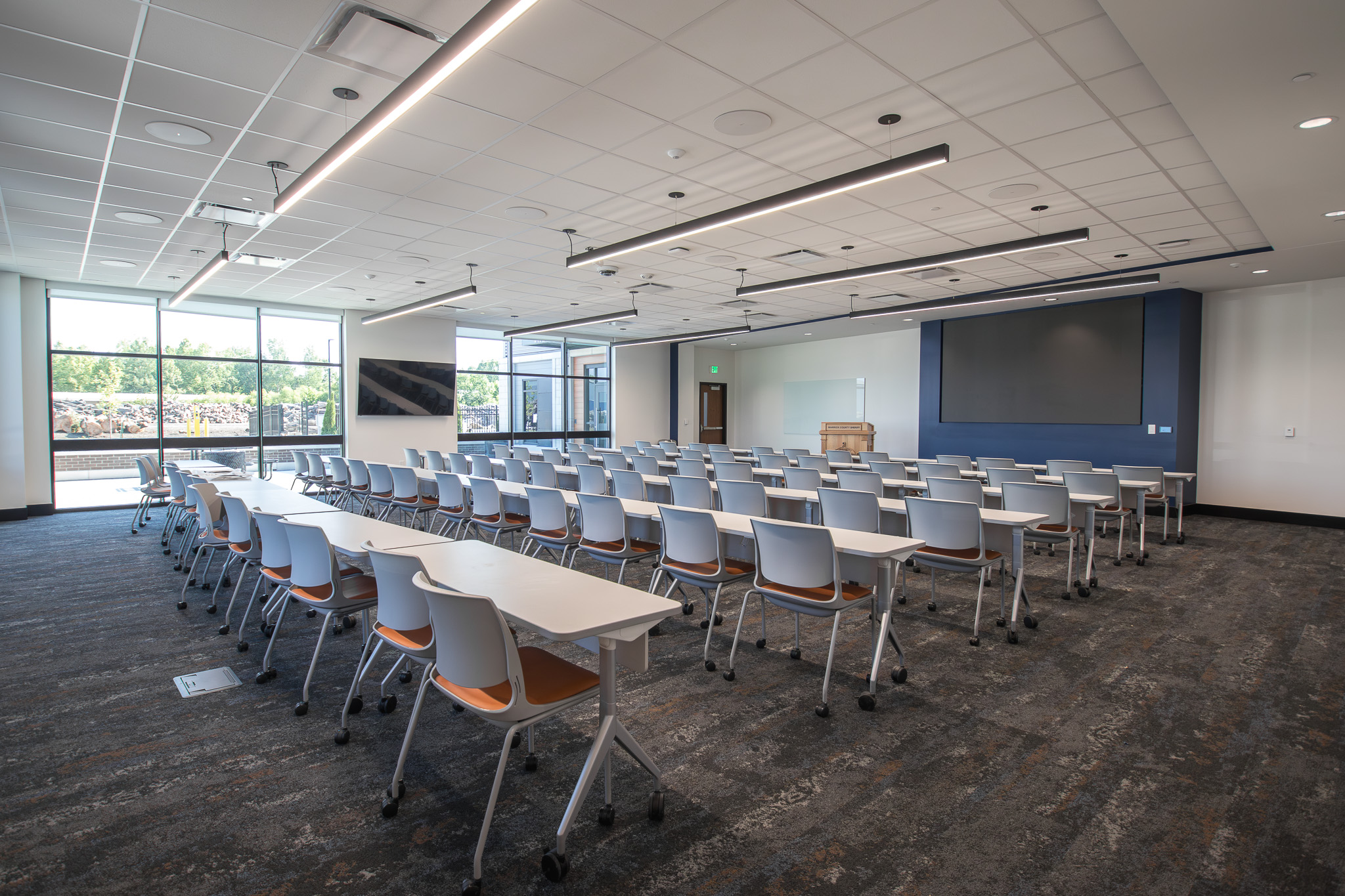 Conference room at the Warrick County facility with rows of tables and chairs, large windows, and wall-mounted displays.