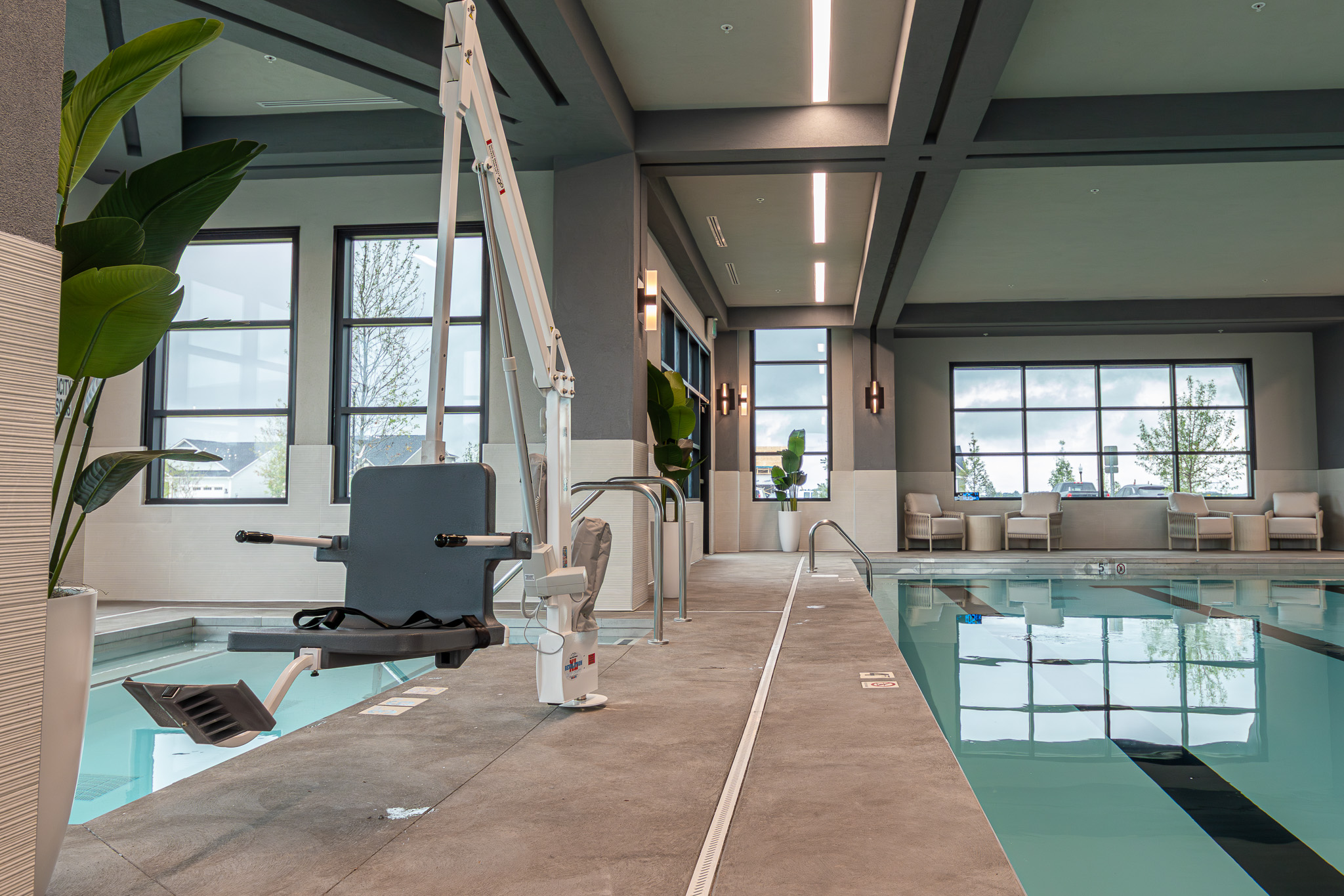 Indoor pool at Del Webb Sagebriar Clubhouse with a pool lift, large windows, and seating areas.