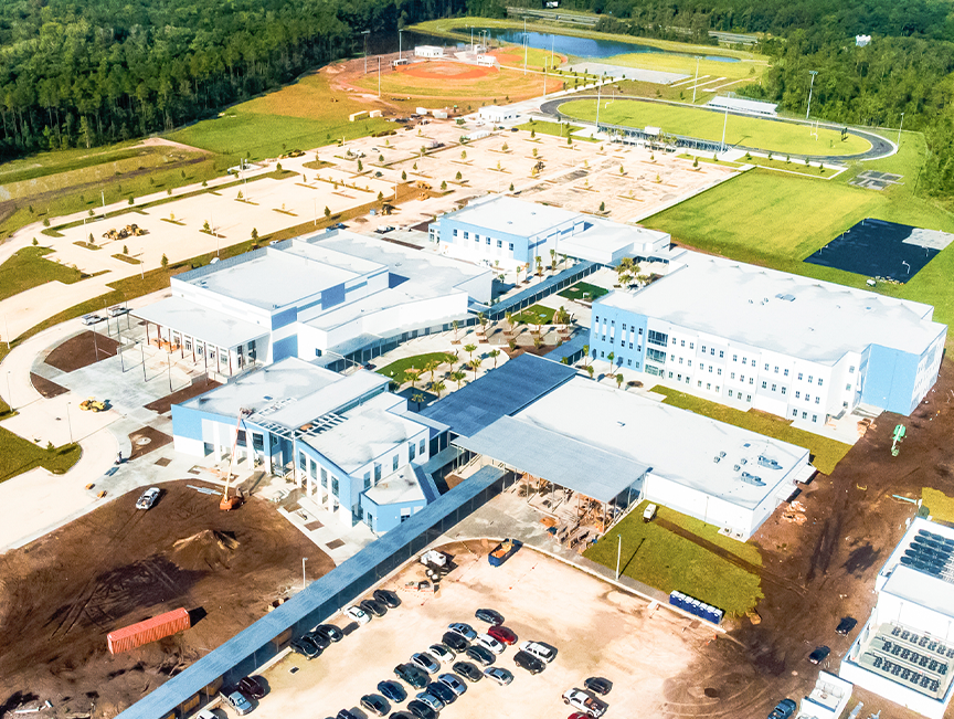 Aerial view of a school campus under construction with classroom buildings, parking areas, athletic fields, and stormwater ponds.
