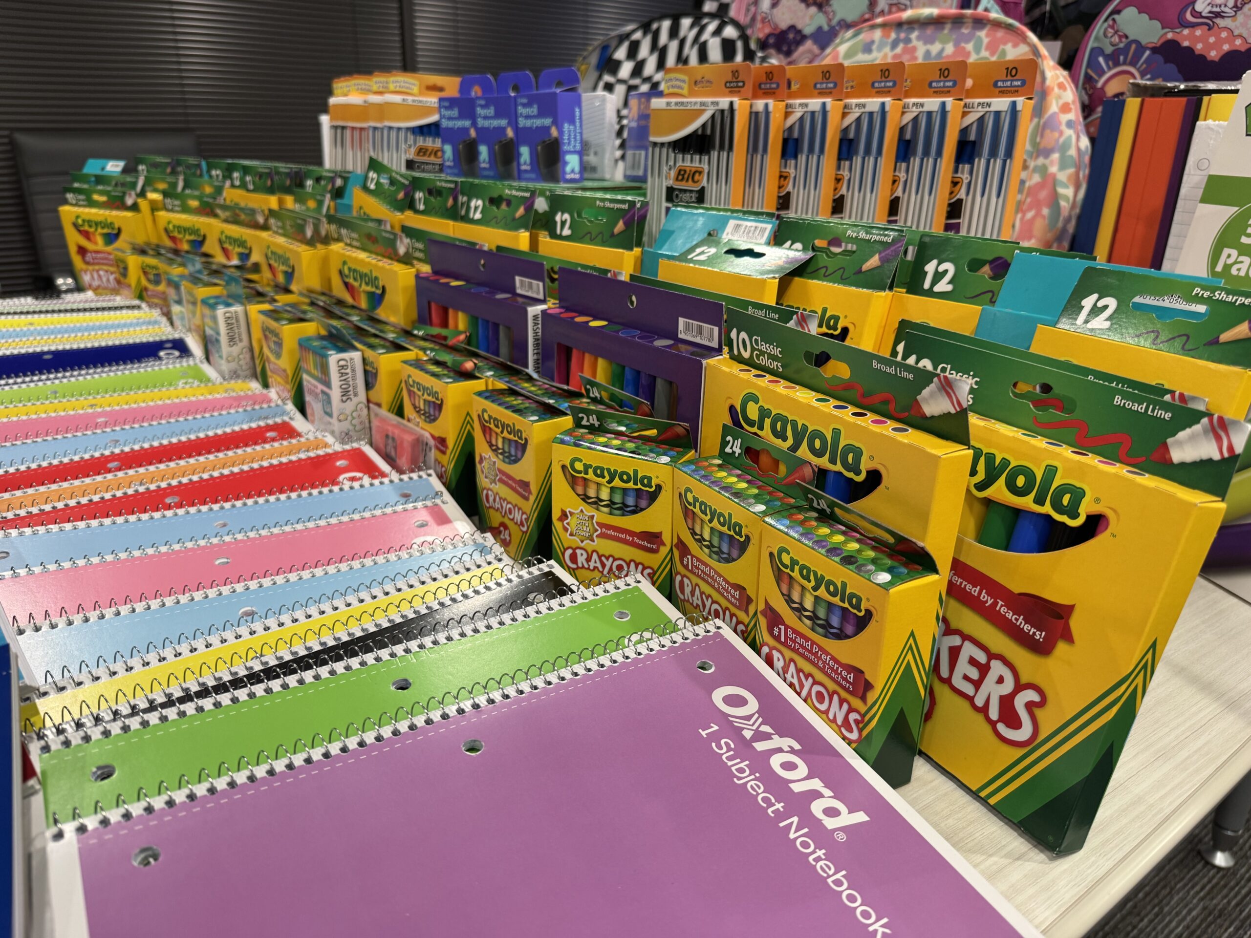 Rows of donated notebooks, crayons, markers, pencils, pens, sharpeners, and backpacks.