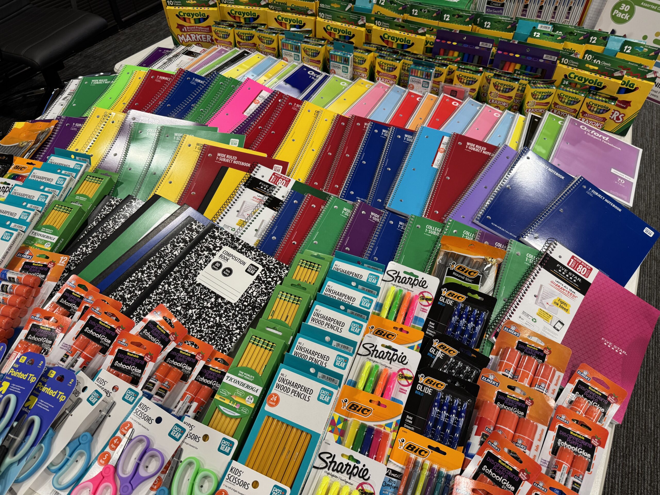 Rows of donated notebooks, crayons, markers, pencils, pens, sharpeners, and backpacks.