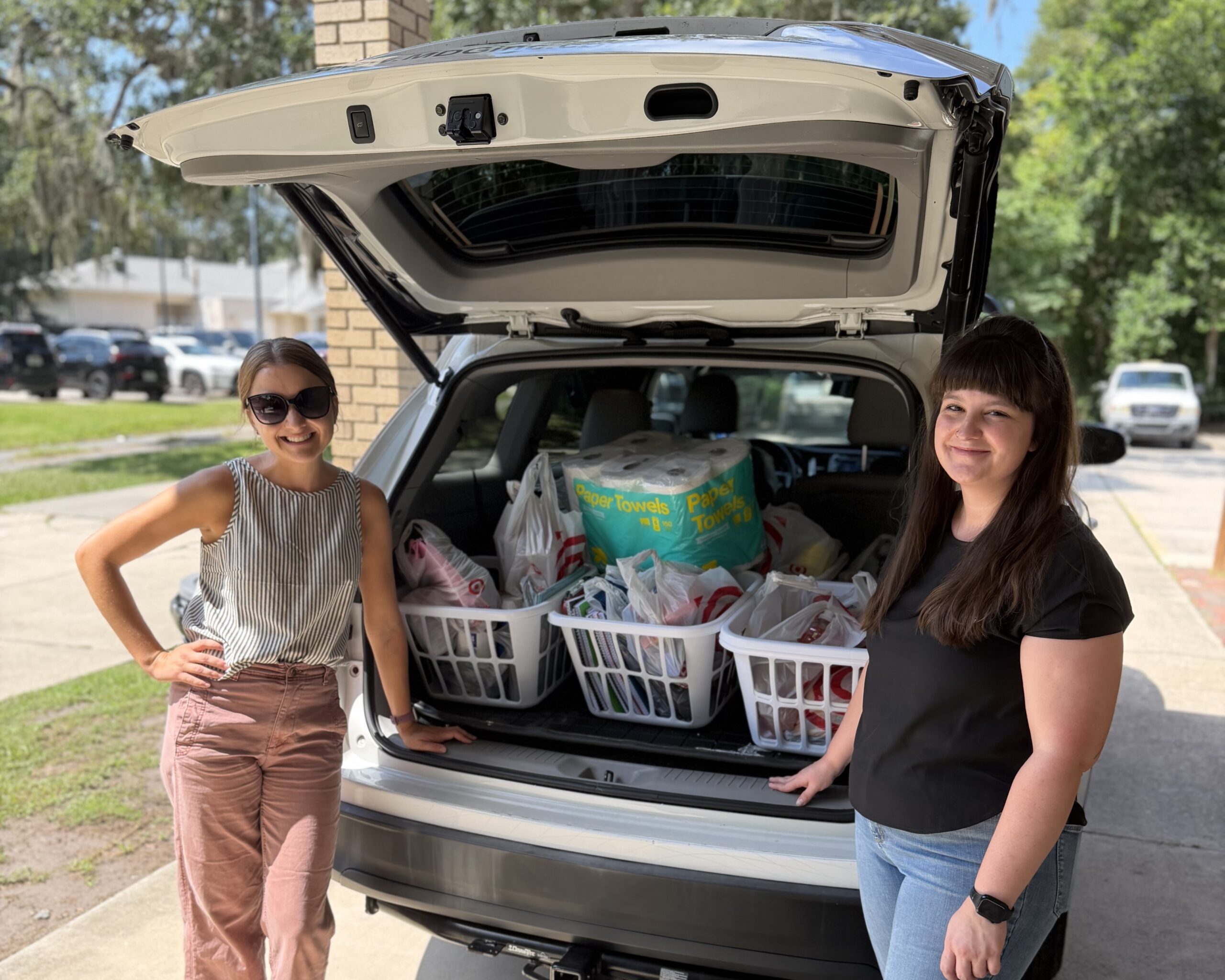 Two DCCM team members standing beside a vehicle filled with donated supplies.