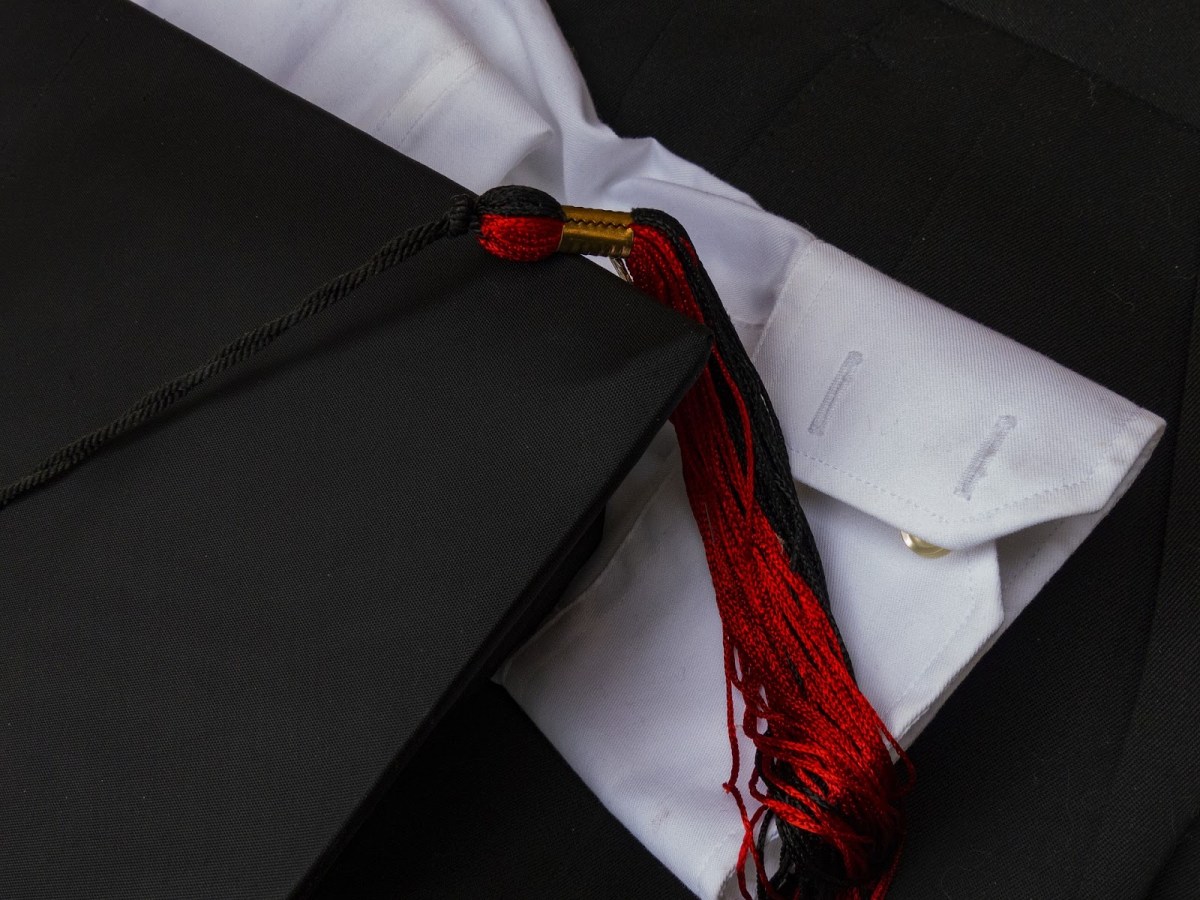 A picture of a graduation cap, tassel, and the cuff of a white dress shirt, reinforcing that a qualified proofreader doesn't need an advanced degree