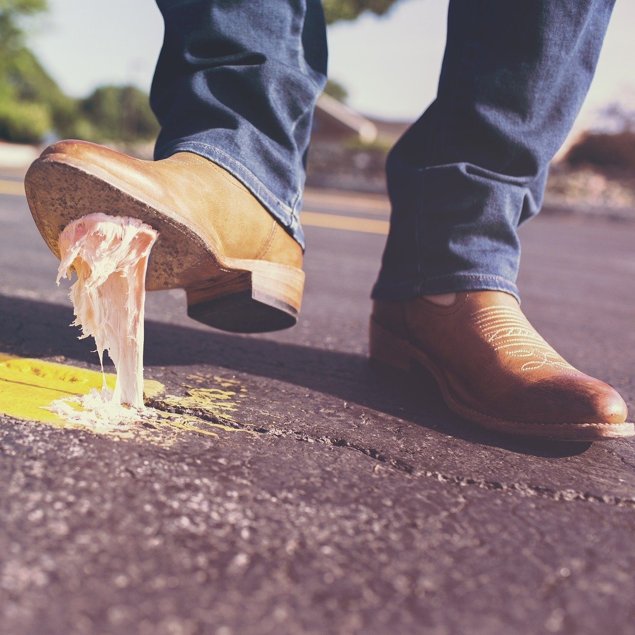 A picture of a man wearing jeans and cowboy boots. He's lifting his right foot and there's gum stuck to it.