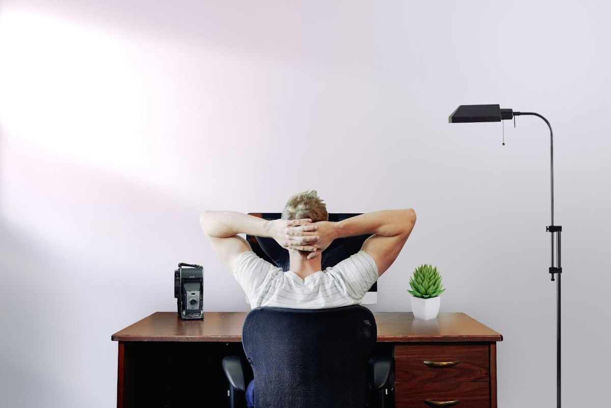 A man sitting at a desk with his hands folded behind his desk, perhaps thinking about how to write a blog
