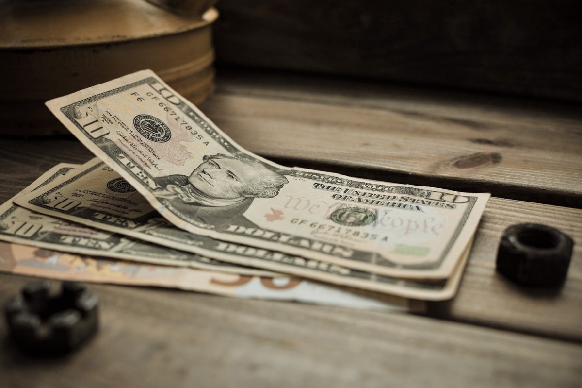 An image of three $10 bills on a slatted wooden table, symbolizing unrealistic copywriting job requirements when it comes to wages.