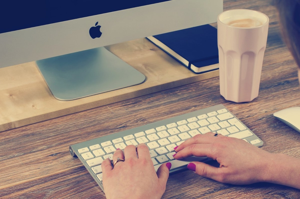 An image of a small, wireless keyboard in front of a Mac monitor, with hands typing.