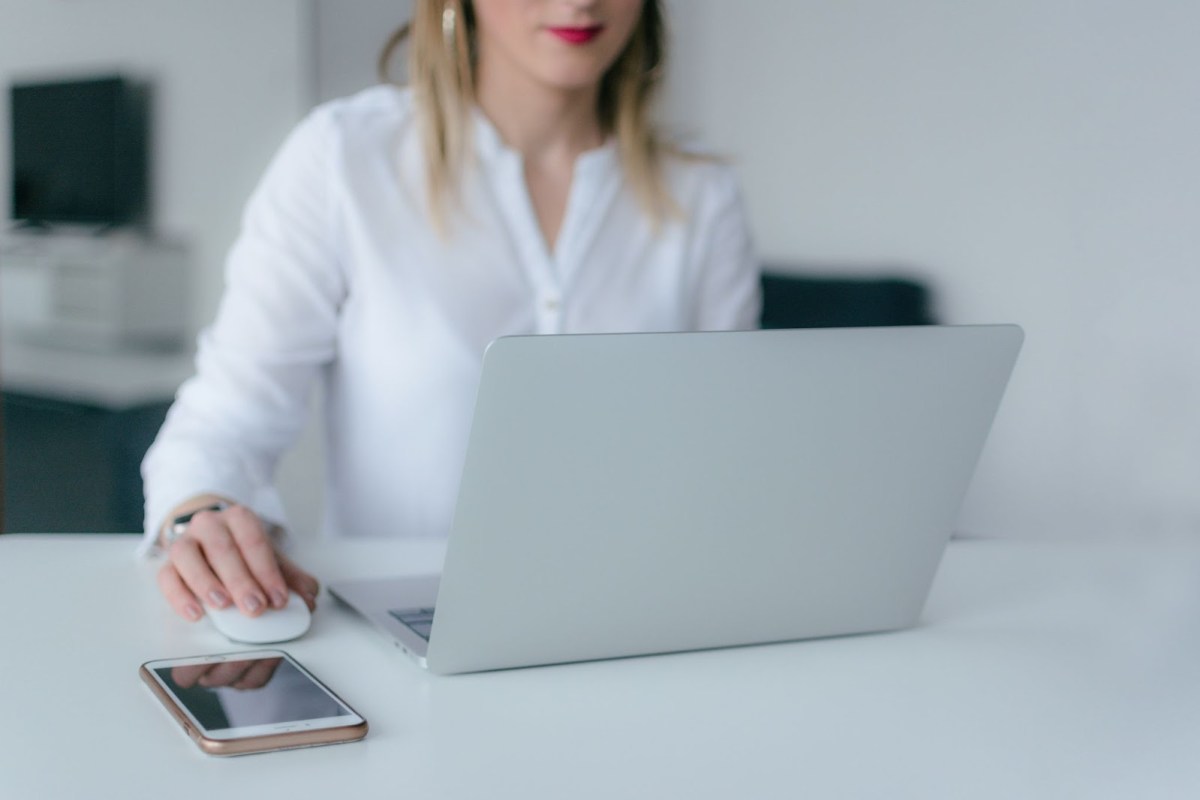 A woman sitting at a desk with a laptop and she is using the mouse