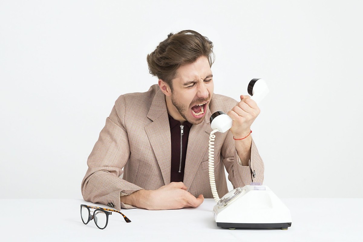 An image of a young man holding a phone receiver in front of as his face as he shouts into the mouthpiece.