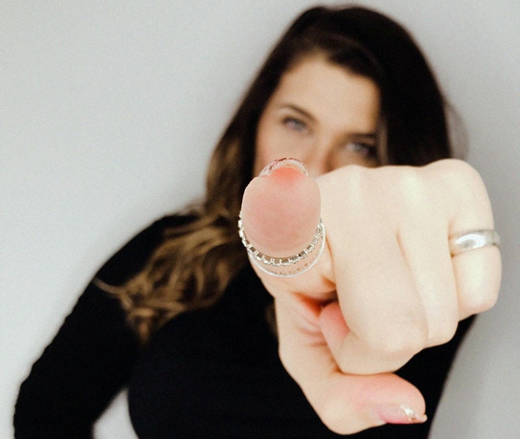 Woman pointing directly at the camera, the tip of her finger is in focus but her face is blurred