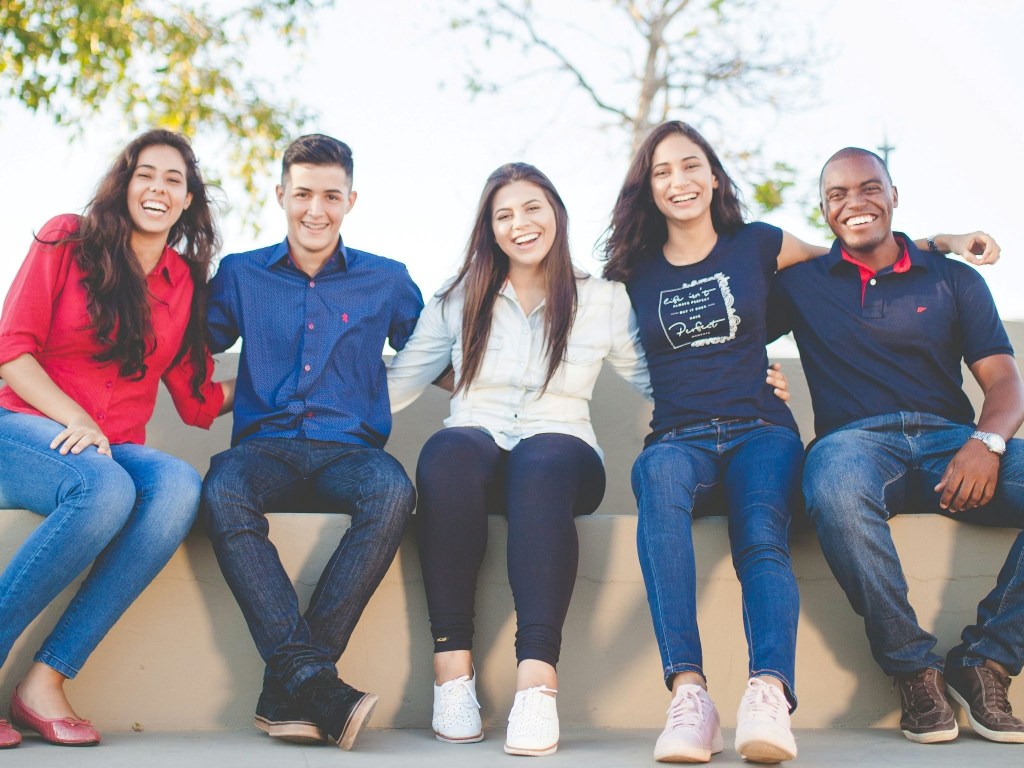 Five people sitting and smiling at the camera, all of various races and ethnicities